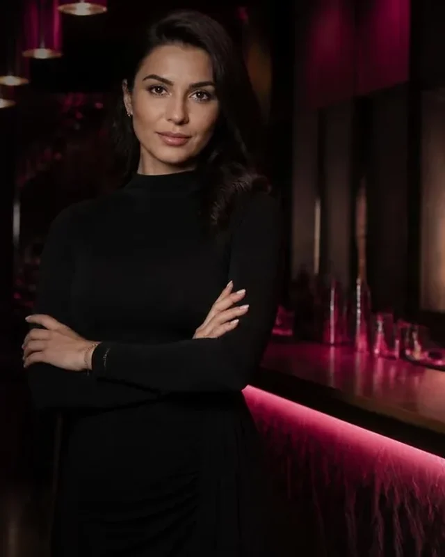 What Fans Are Really Paying For: Girls Lounge cover image showing an elegant woman in a long-sleeved black dress in a lounge bar, neon pink lighting (AI-generated illustration)