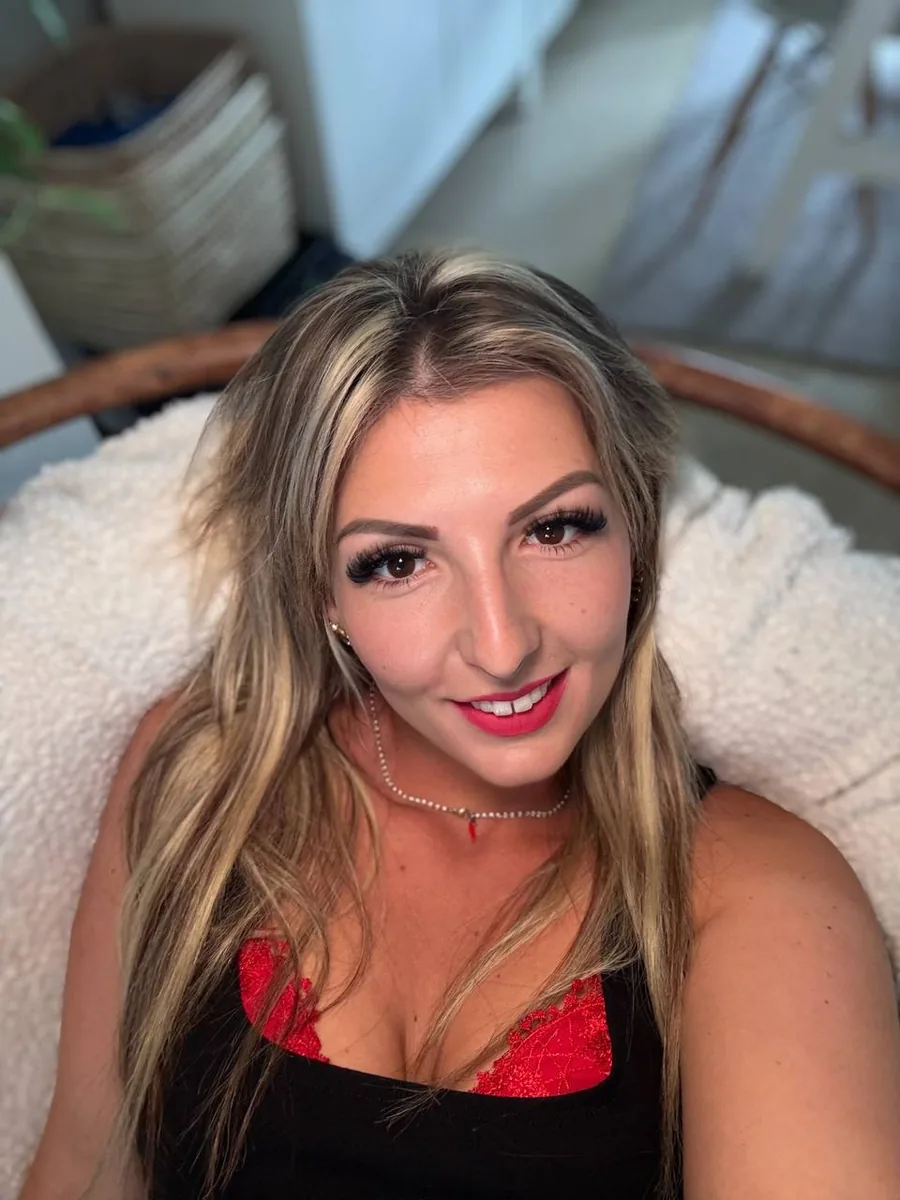 Capucine_porno smiling in a black top with red lace trim, close-up selfie
