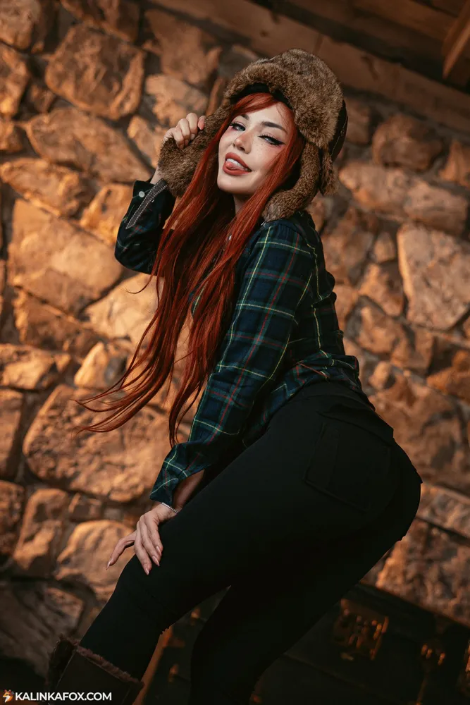 Kalinka Fox with long red hair in a flannel shirt, forest backdrop